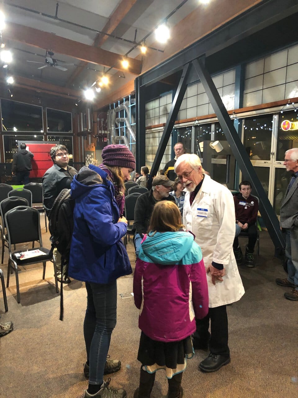 Older man in a white lab coat talking to a teenager and a child.